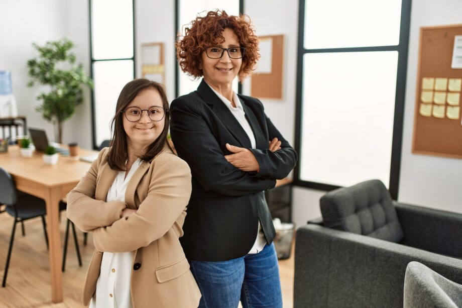 Group of two women working at the office. Mature woman and down syndrome girl working at inclusive teamwork.