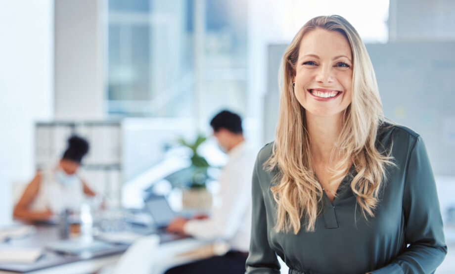 Female leader, manager or CEO with a smile, mission and vision in the office and her team in the background. Leadership, management and success with a woman boss and corporate business people at work.