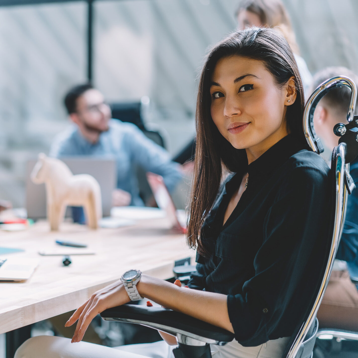 Portrait of Asian prosperous employee sitting front laptop computer at meeting table with male and female colleagues collaborating on blurred background, female office worker satisfied with her job