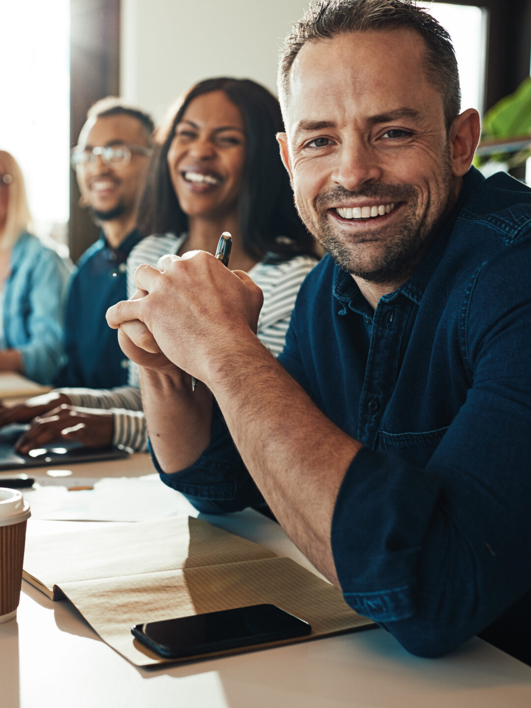 Smiling businessman sitting with a diverse group of coworkers during a meeting together at a table in an office